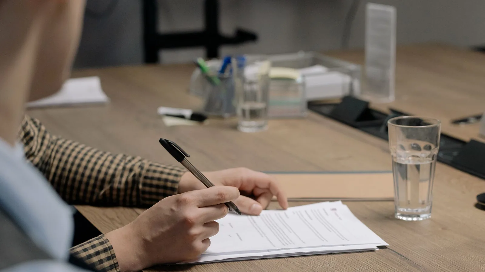 Personne en tenue professionnelle signant un document sur une table en bois